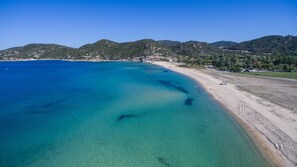 A coastal beach with clear turquoise waters, sandy shore, and hills in the background. - Camping  Pitsoni (Sithonia)