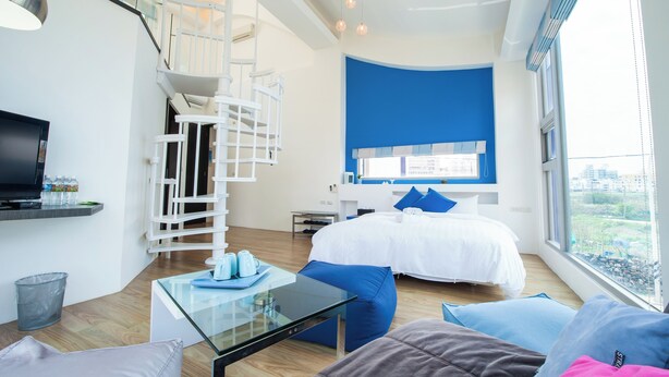 Ein modernes Hotelzimmer mit Bett, Glastisch, Fernseher, einer Treppe und Blick auf die Stadt.