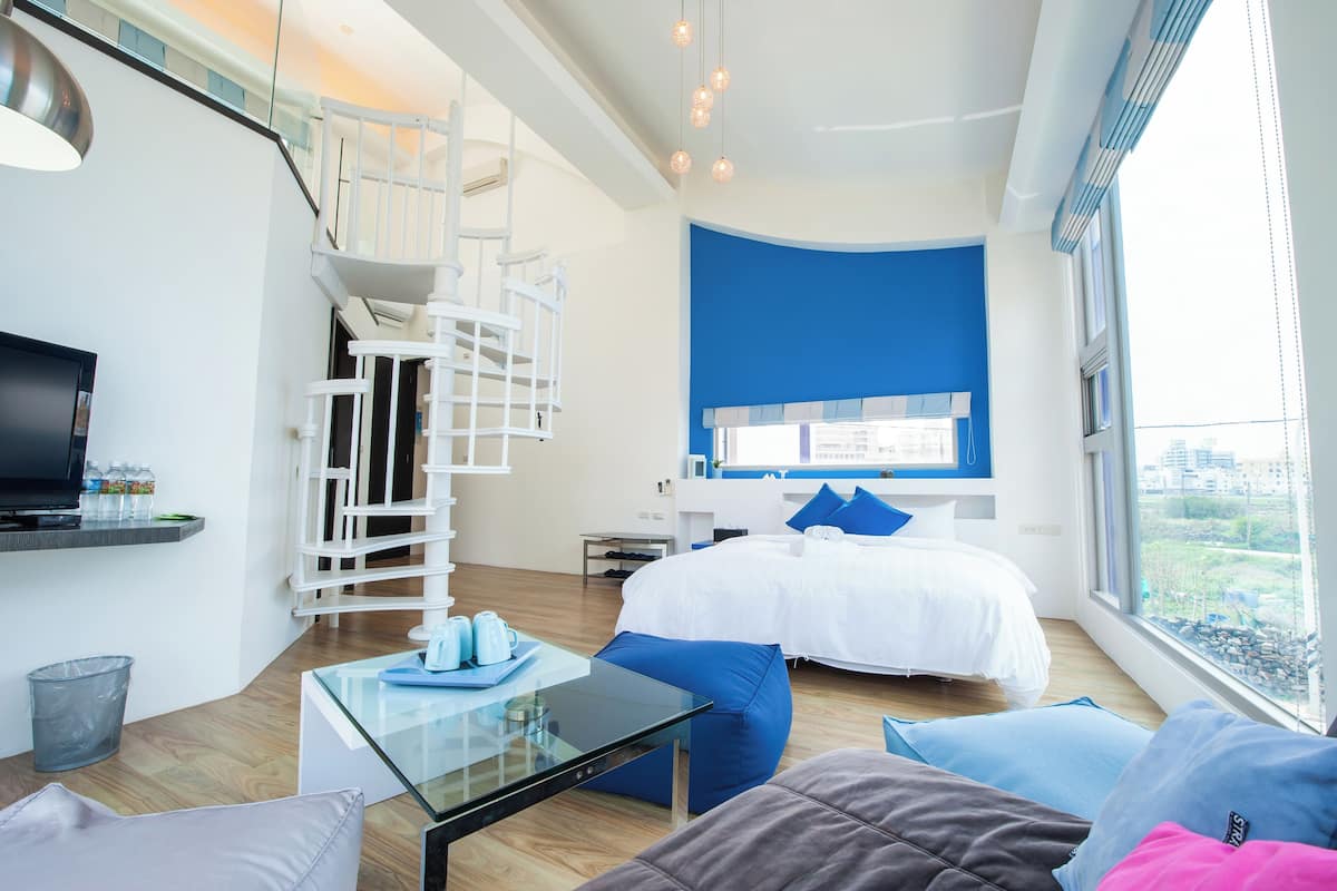 Une chambre d’hôtel moderne avec un lit, une table en verre, un téléviseur, un escalier et une vue sur la ville.
