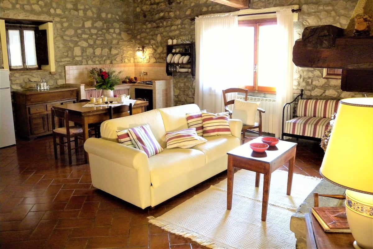 Una sala de estar acogedora con sofá, una mesa de comedor y una zona de cocina con paredes de piedra y vigas de madera.