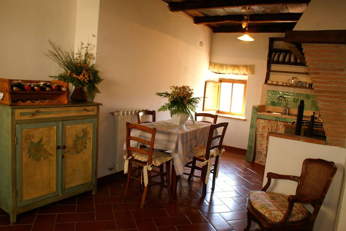 Comedor con una mesa dispuesta para cuatro personas, rodeada de sillas de madera. Se ve un aparador con botellas de vino a la izquierda.