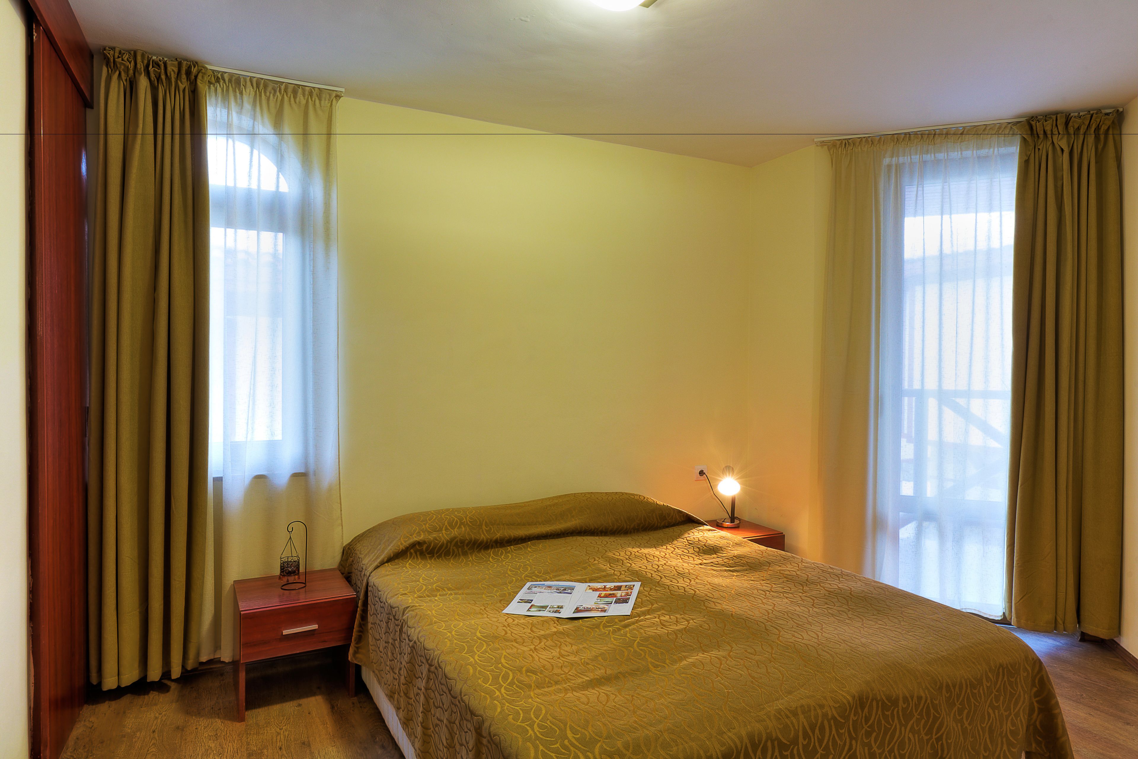 A hotel room with a bed, a nightstand, a lamp, and curtains.