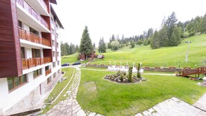 Un hotel de varios pisos con balcones, un camino de piedra, un jardín ajardinado y un paisaje montañoso de fondo.