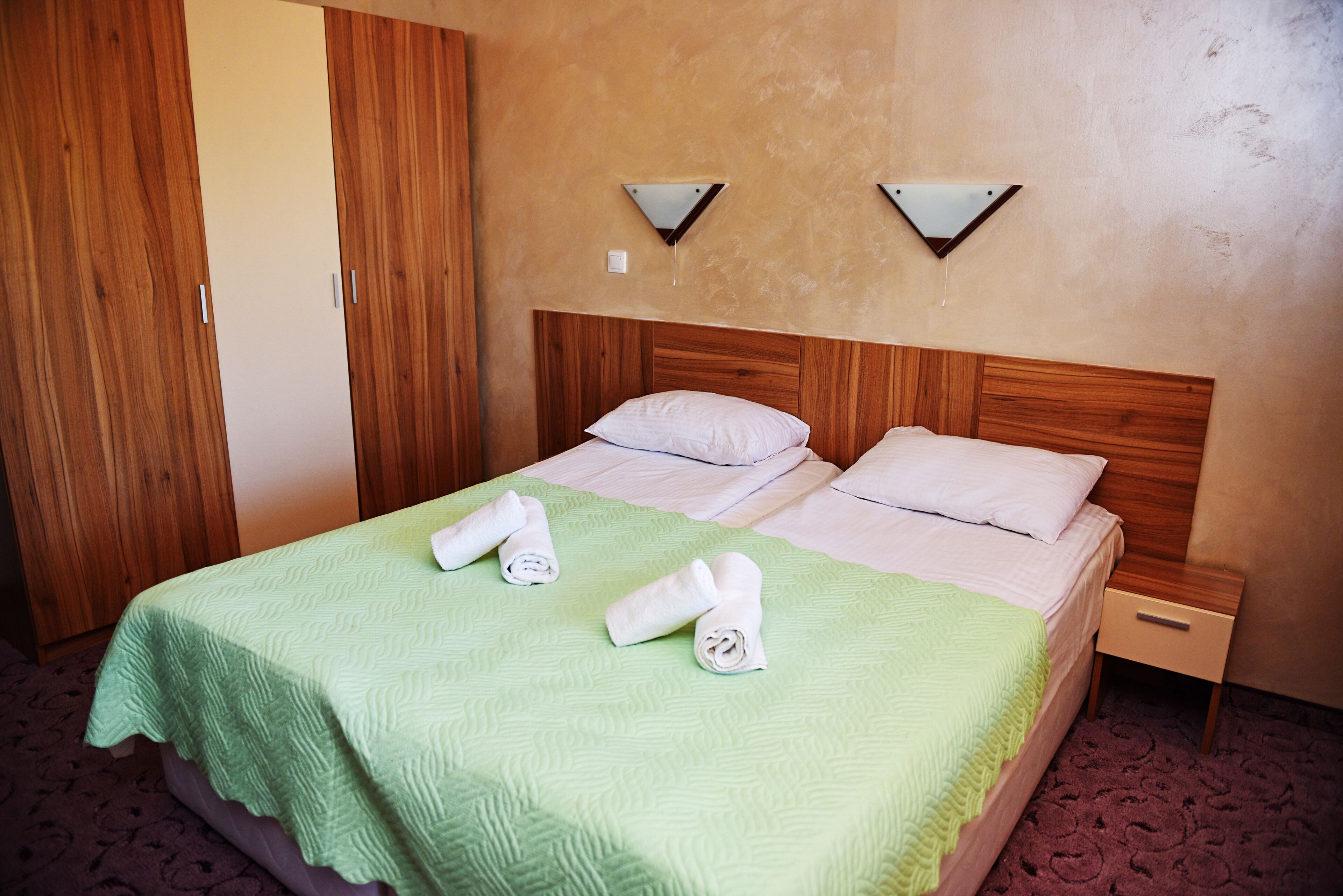 Une chambre d’hôtel avec un lit, deux tables de chevet, une armoire en bois et une couvre-lit verte.