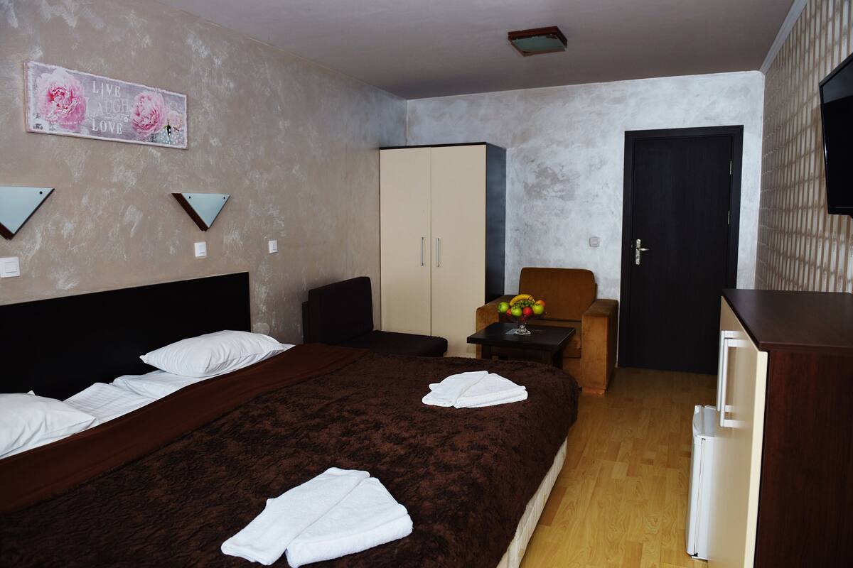A hotel room with a bed, a wardrobe, a small table with fruit, and a TV on the wall.