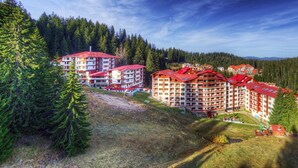 Un complejo hotelero con varias construcciones, rodeado de un bosque denso y colinas.