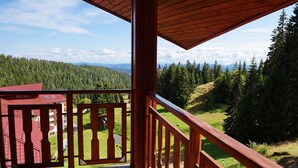 Un balcón de madera con vistas a un valle boscoso y montañas distantes.