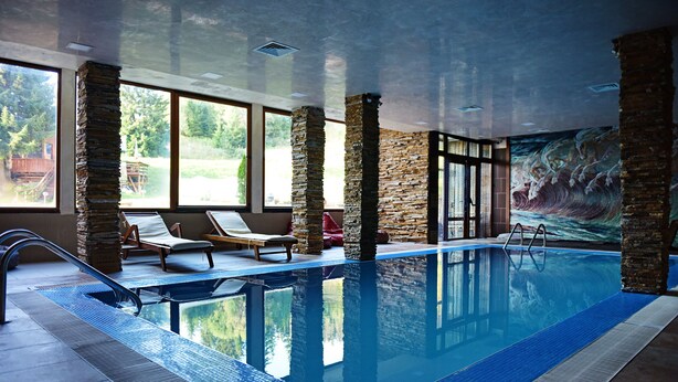 Una piscina interior con pilares de piedra, sillones de descanso y un mural en la pared.