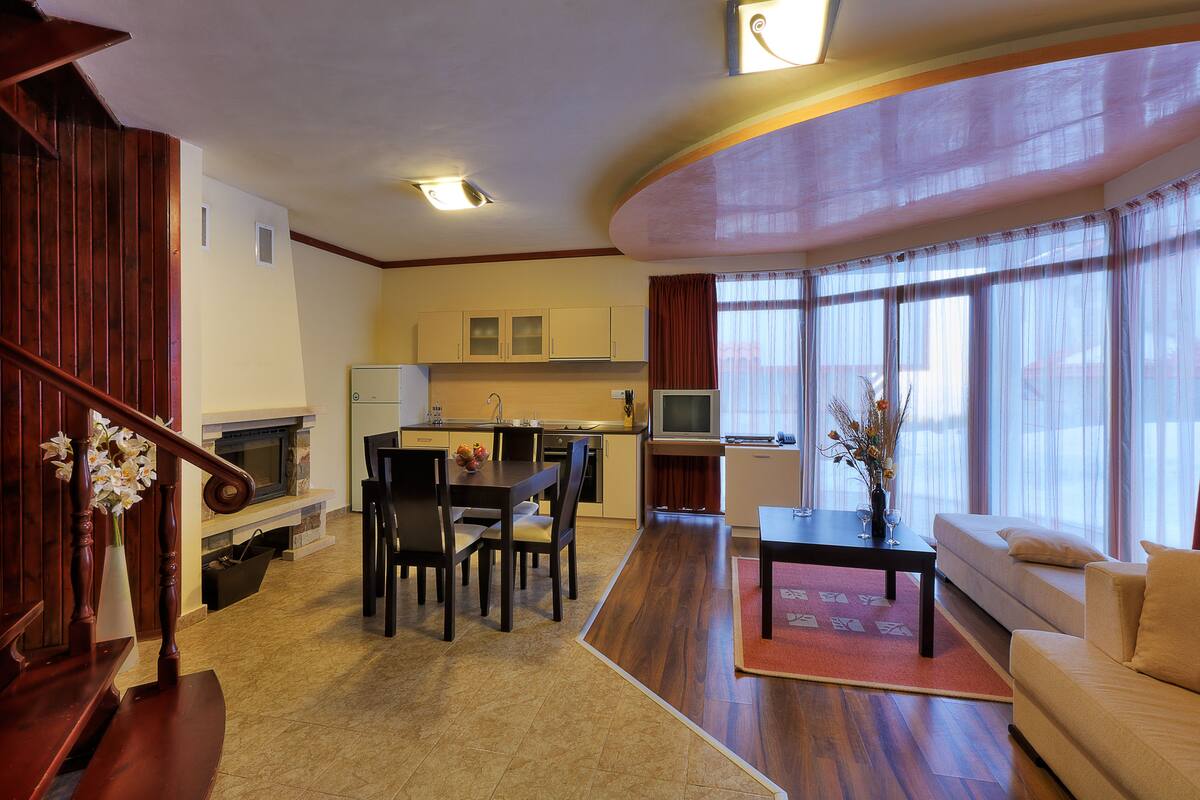 A spacious living area with a dining table, sofa, and a kitchen in the background.