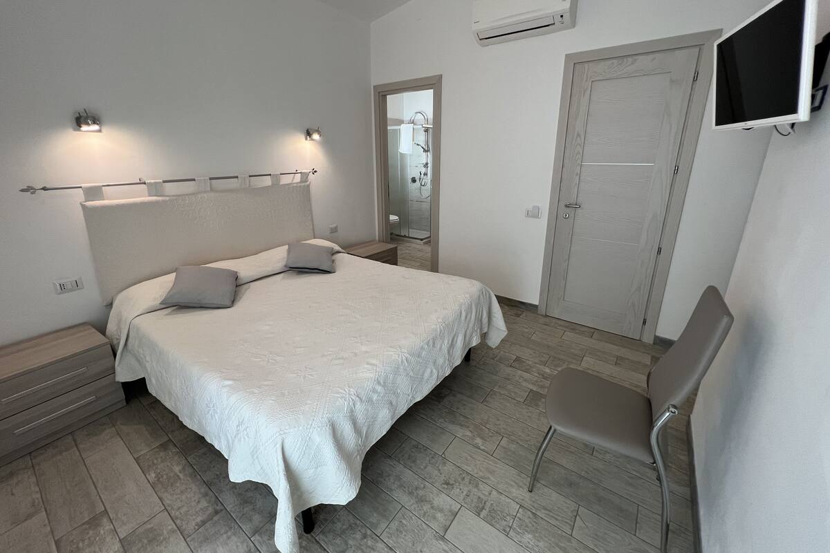 Camera da letto con un letto, comodini, una sedia, un condizionatore d'aria e una televisione.