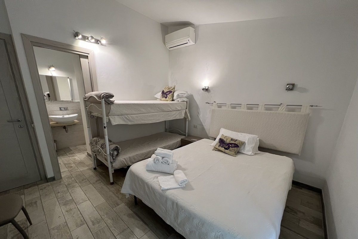 Una camera da letto con un letto a castello, un letto singolo, un bagno con un lavandino e un condizionatore d'aria.