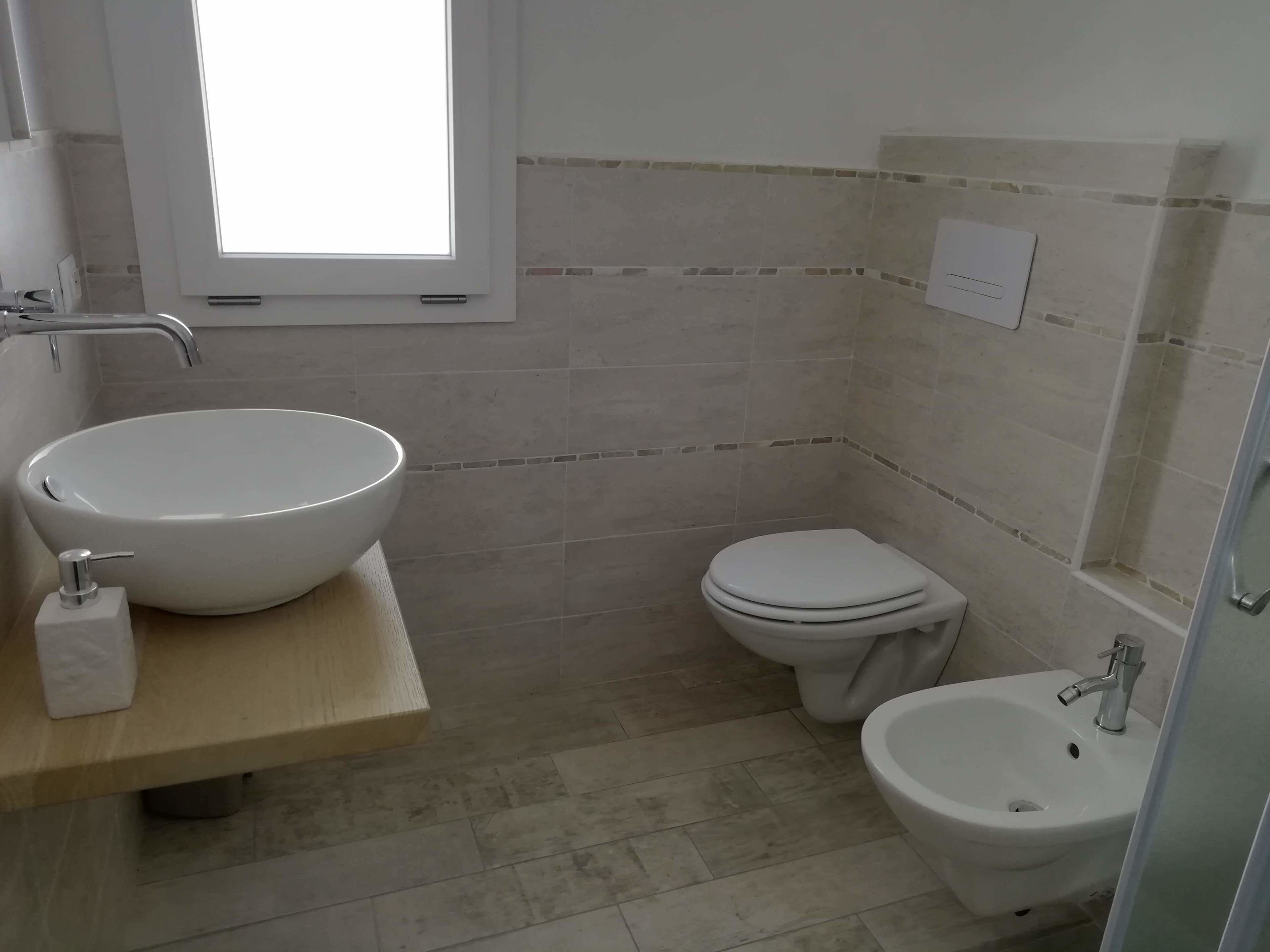 A bathroom with a large vessel sink, a toilet, and a bidet.