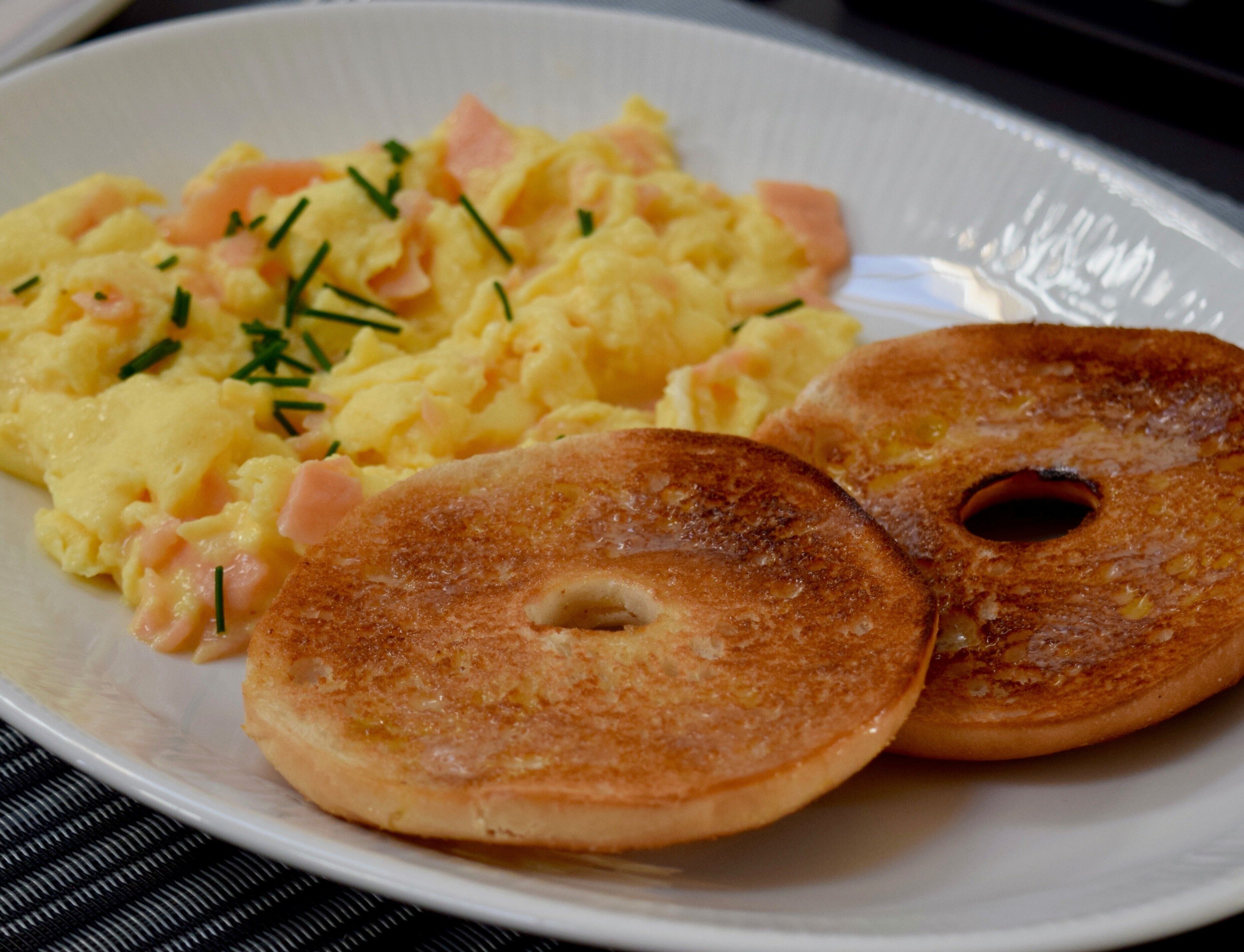 A plate with scrambled eggs, ham, and chives, and two golden-brown bagels.