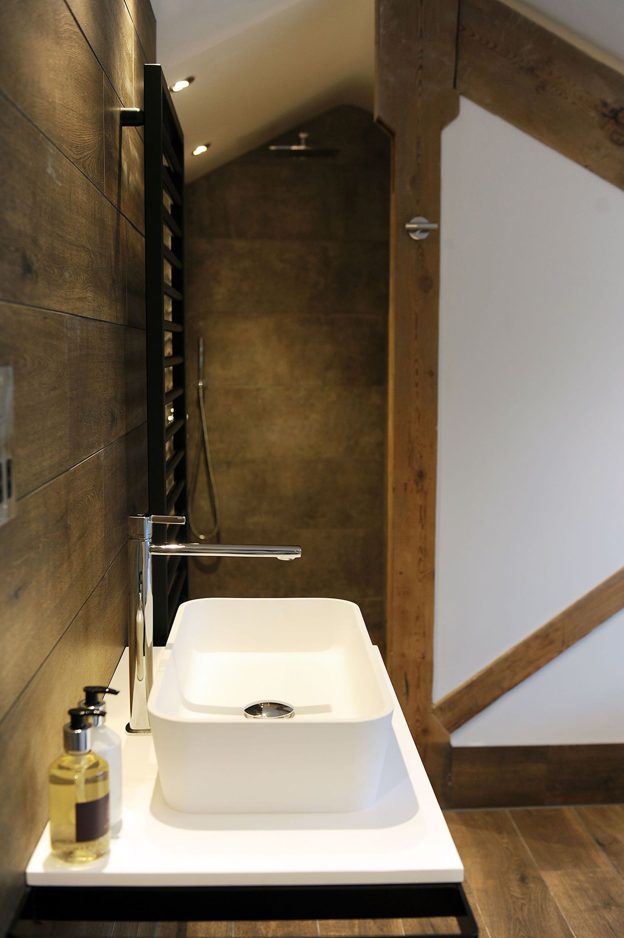 A modern bathroom with a white sink, wooden walls, and a shower area.