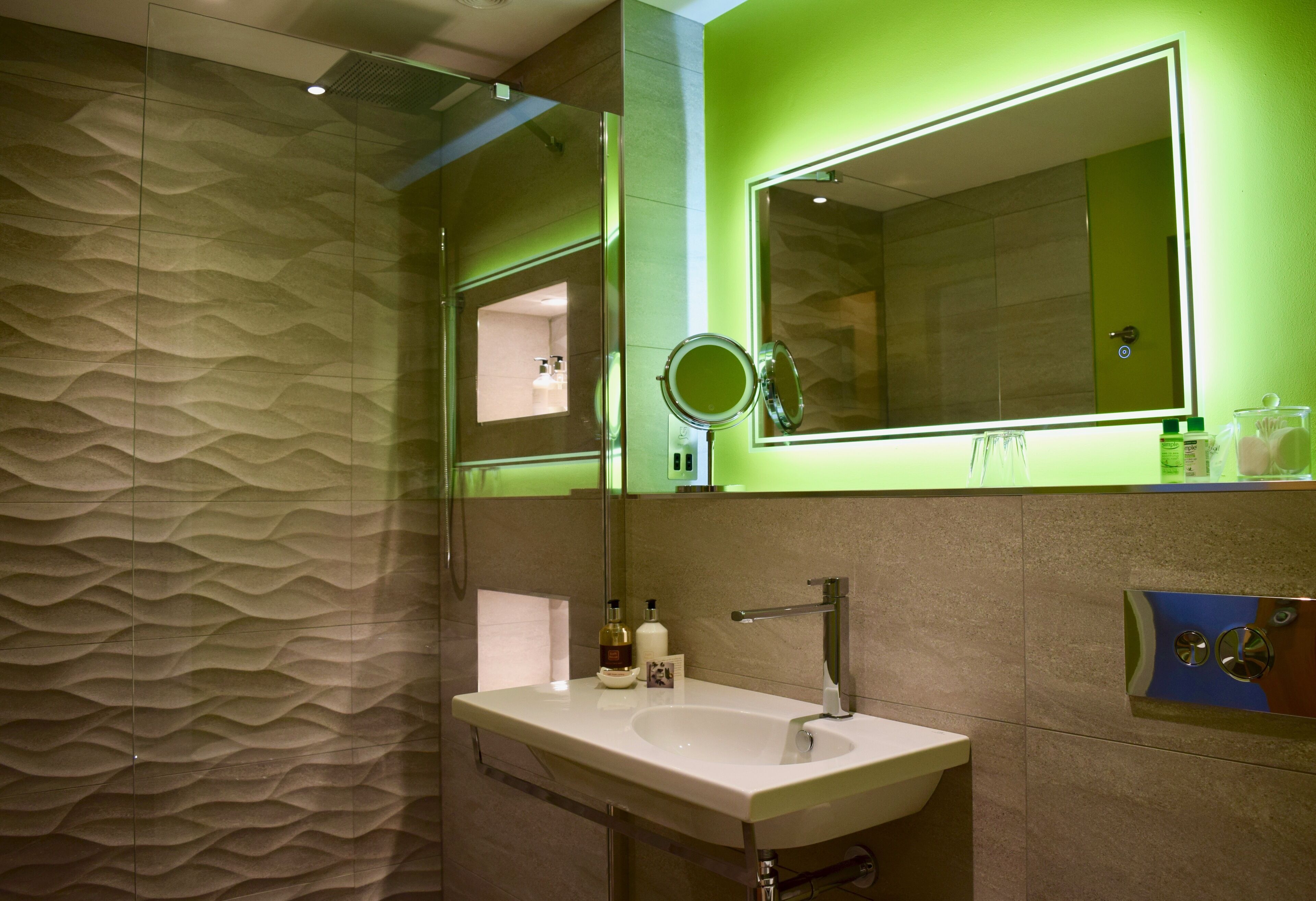 A modern bathroom with a textured wall, a large mirror, and a sink with a faucet.