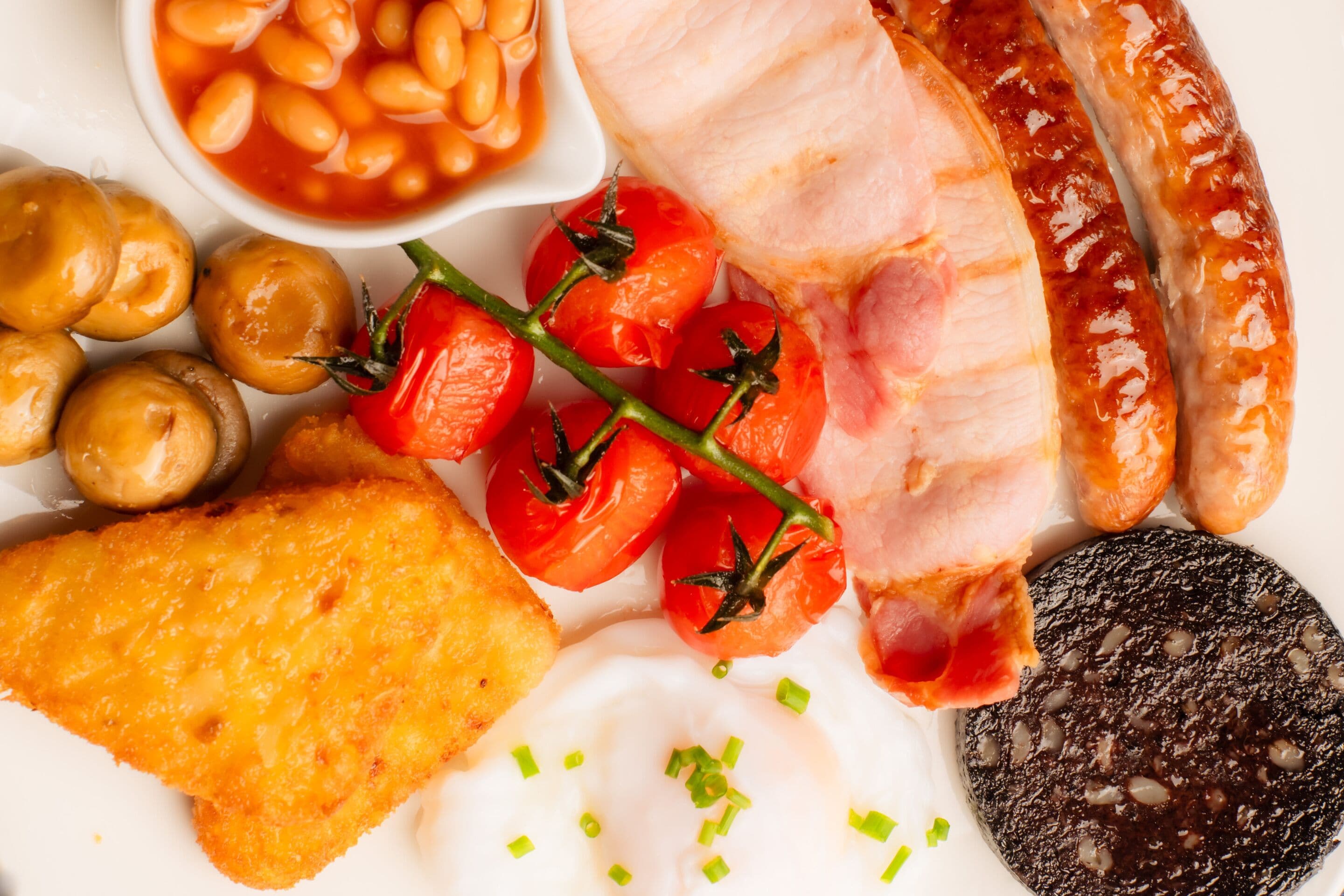 A plate of food including sausages, tomatoes, beans, mushrooms, and a slice of black pudding.