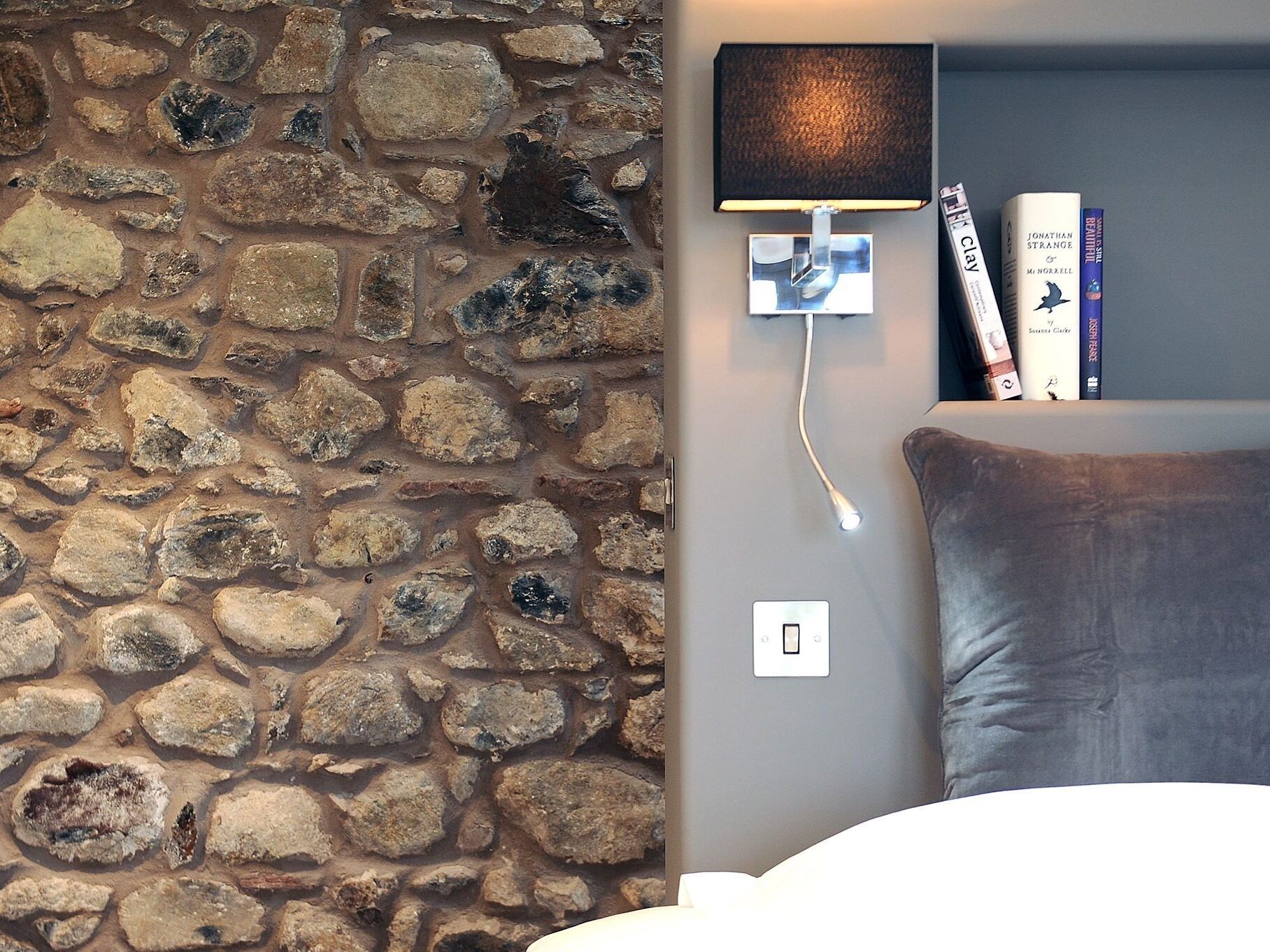 A stone wall, a modern lamp, a power outlet, and a bookshelf with books.