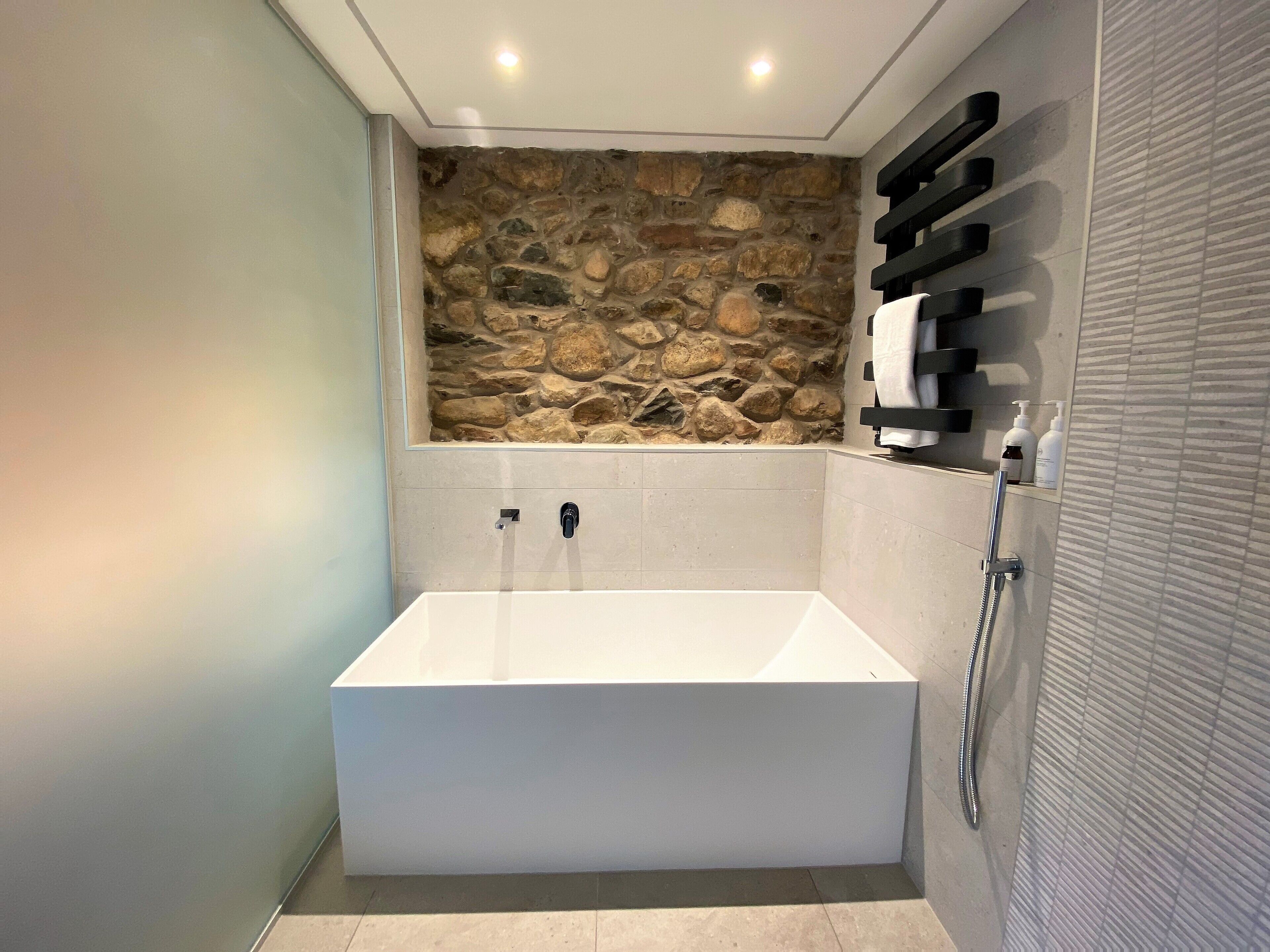 Une salle de bain moderne avec un mur en pierre, une baignoire blanche et un espace douche.