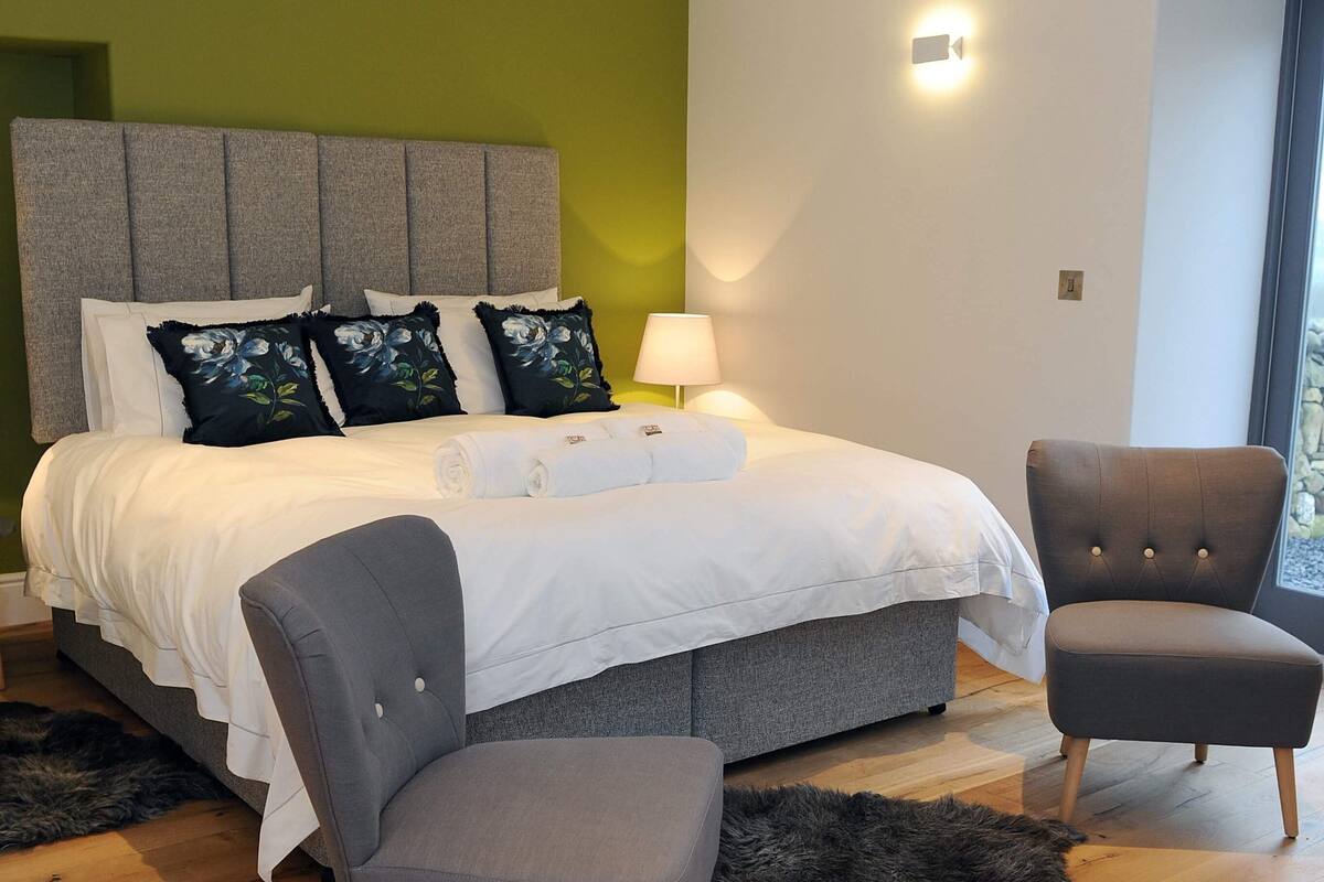 A bedroom with a bed, two chairs, a rug, and a lamp.