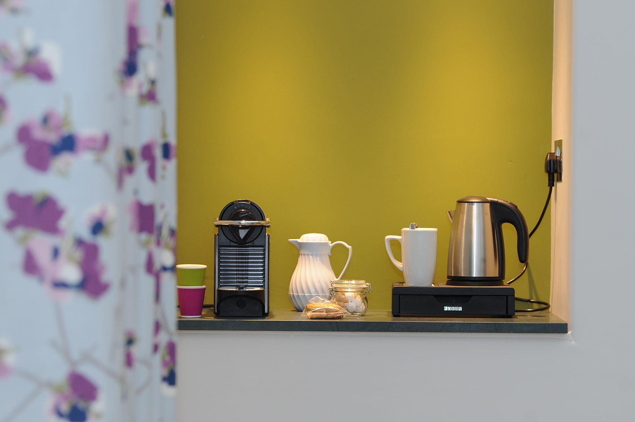 A kitchen counter with a coffee maker, a kettle, a teapot, and a jar of cookies.