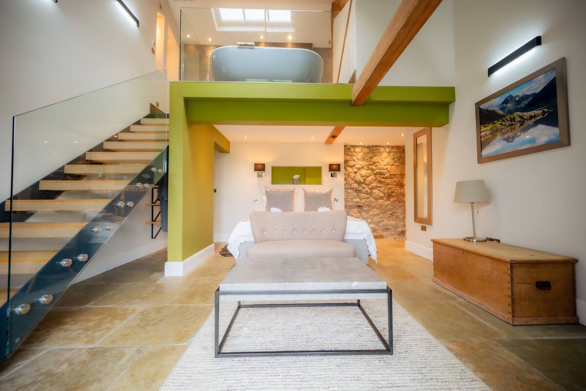 A modern interior with a staircase, a bed, a stone wall, and a painting.