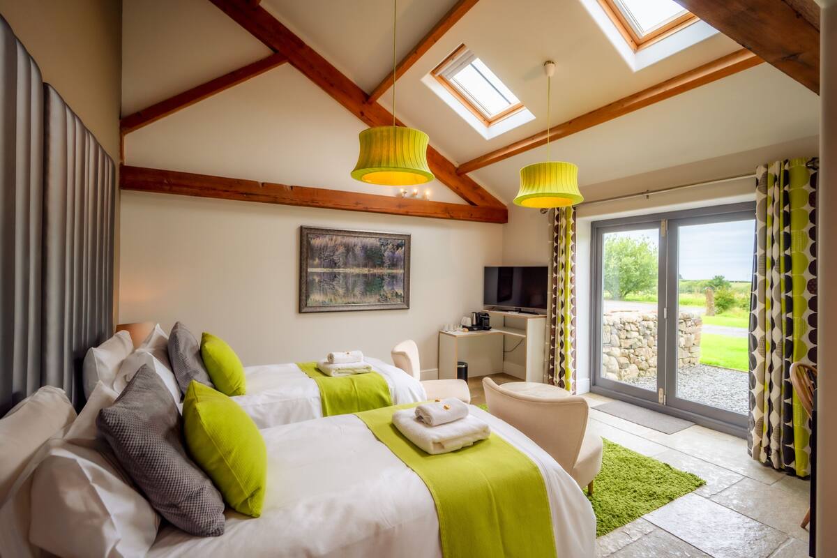 A hotel room with two beds, a desk, a TV, and a large sliding glass door to the outdoors.