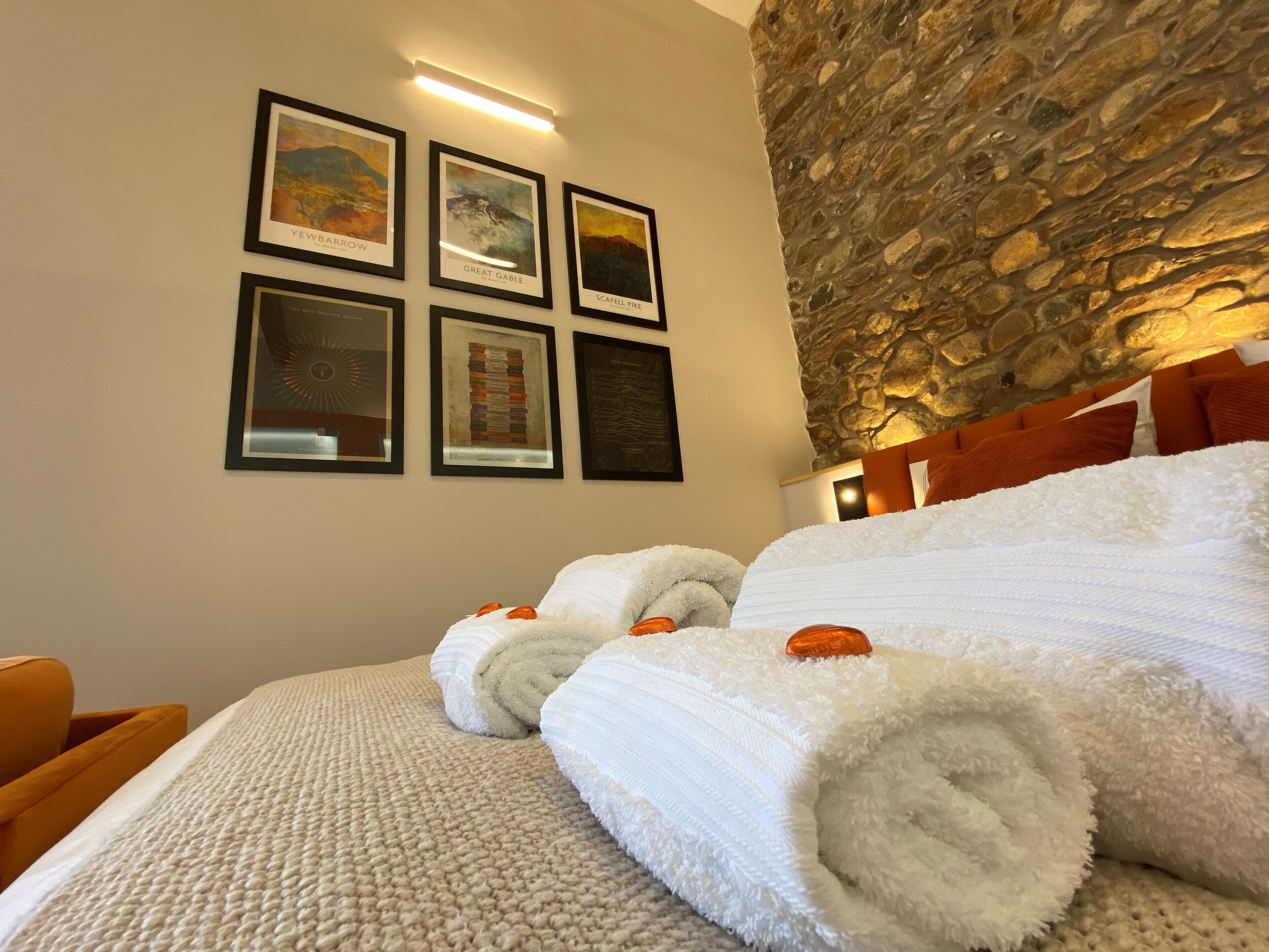 A hotel room with a stone wall, a bed with white linens, and four framed artworks on the wall.