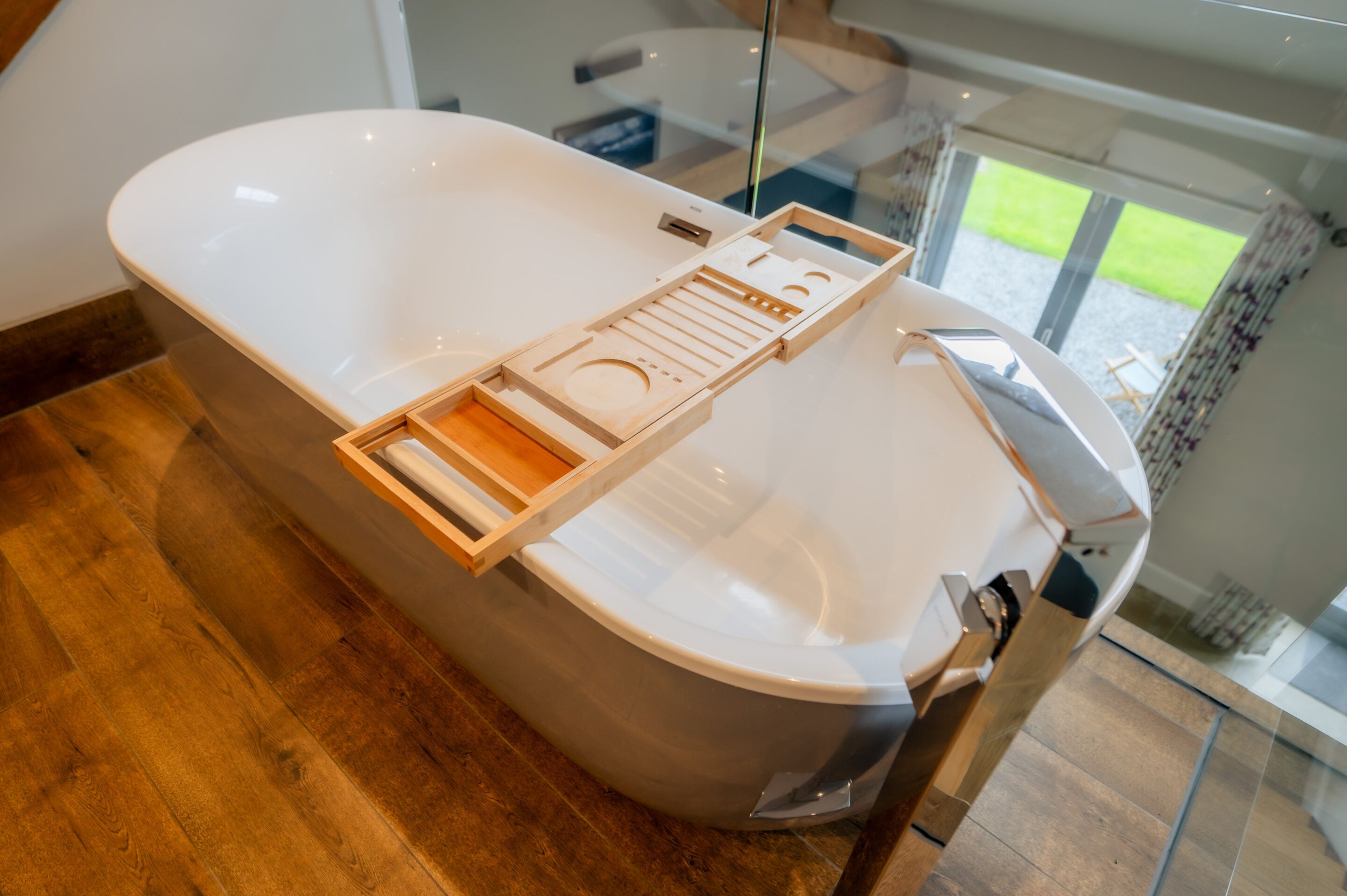 Une salle de bain moderne avec une grande baignoire, un plateau en bois pour y poser des accessoires pendant le bain et une cabine de douche en verre.