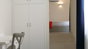 Una habitación con cama, escritorio, silla, armario y una escalera que lleva a un baño.