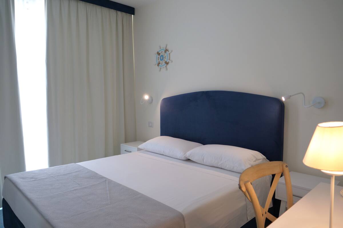 A hotel room with a bed, a nightstand, a chair, a lamp, and a wall decoration.