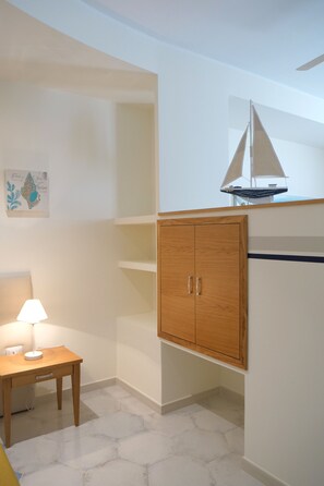 Una habitación con un armario de madera, una mesita con una lámpara y un modelo de velero encima del armario.
