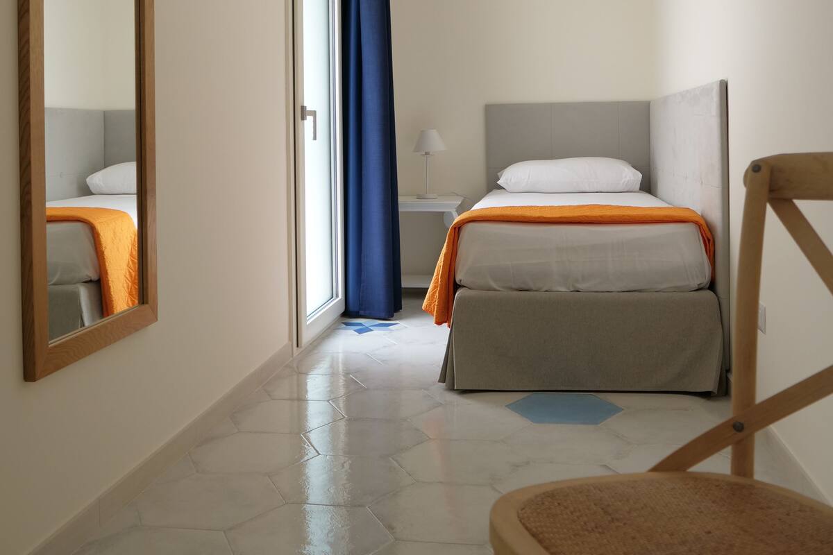 A hotel room with a bed, a chair, a mirror, and a door leading to another room.