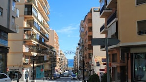 Calle con edificios de varios pisos, cielo despejado y algunos coches estacionados.