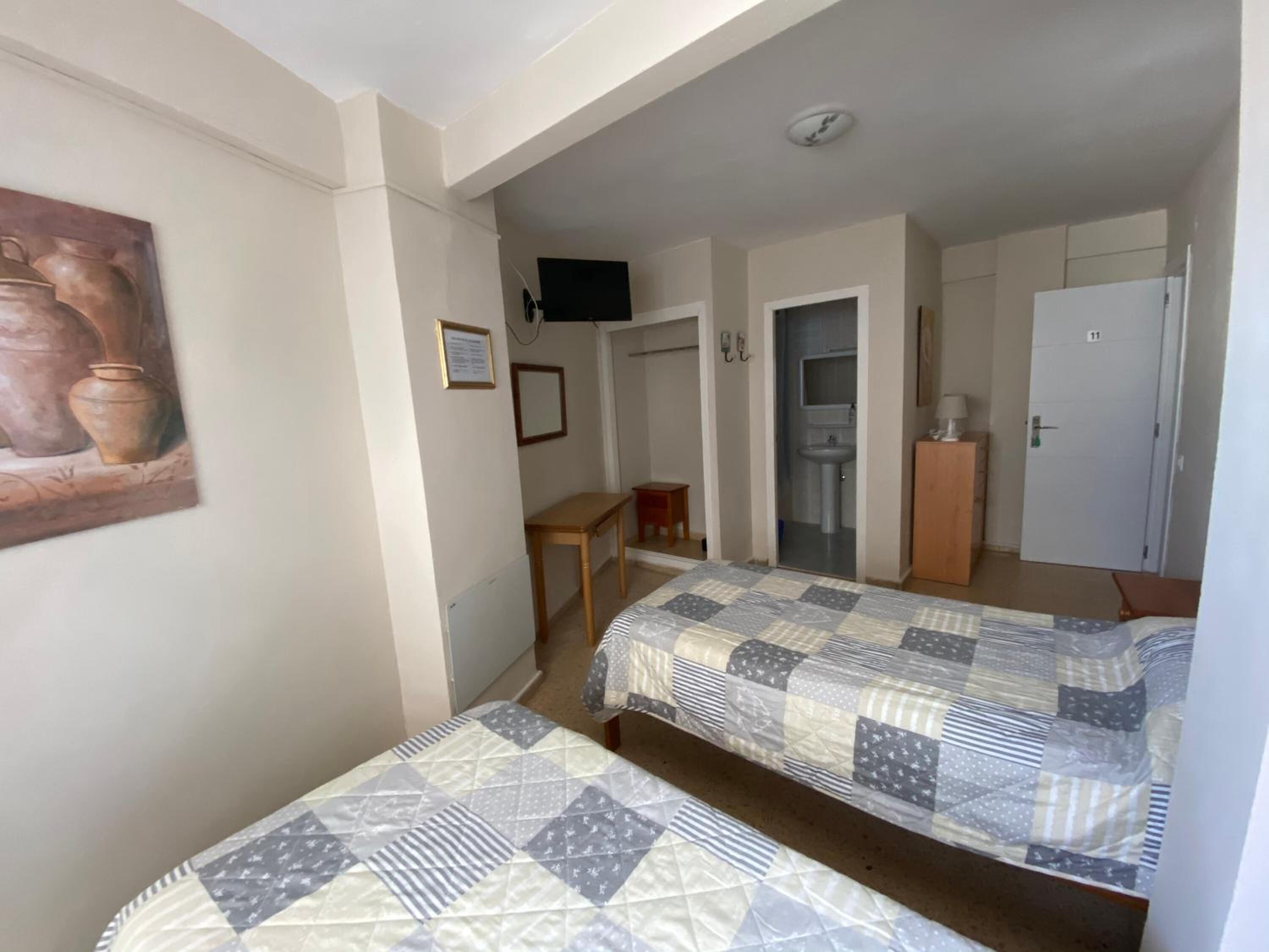 Ein Zimmer mit zwei Betten, einem Schreibtisch, einem Stuhl, einem Fernseher und einer Tür zu einem Badezimmer.