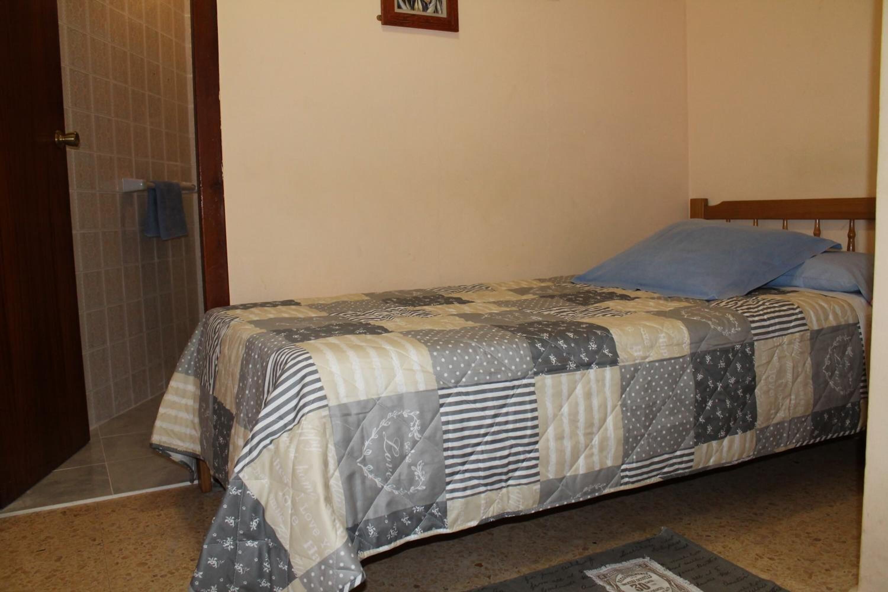 Un dormitorio con una cama cubierta por un edredón de retazos, un cabecero de madera y una alfombra pequeña en el suelo.