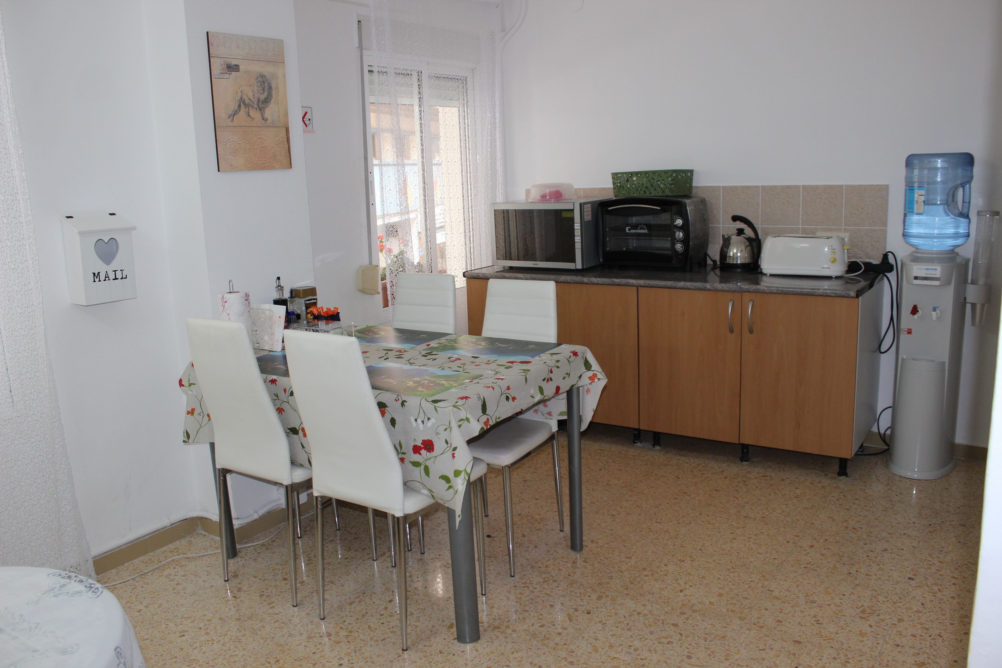 Una cocina pequeña con una mesa de comedor, sillas, microondas, tostadora y dispensador de agua.
