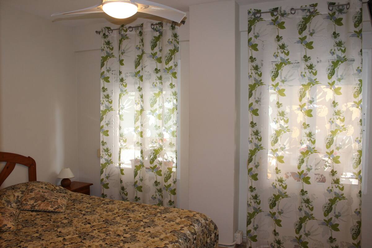 A bedroom with a bed, a nightstand, a lamp, and a ceiling fan.