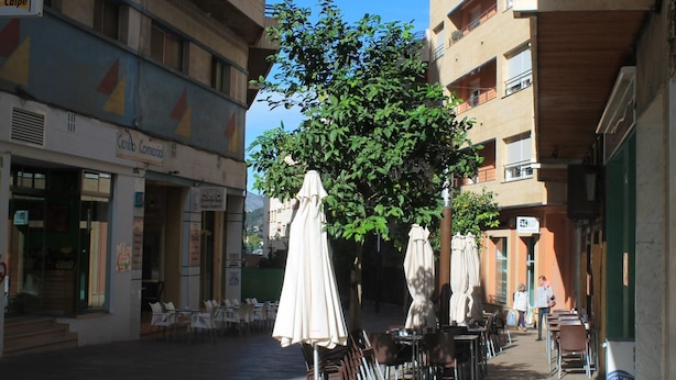 Un área de café al aire libre con mesas y sillas, sombrillas y un árbol que da sombra.