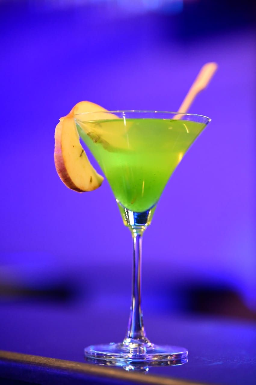 Una copa de martini con un líquido verde y una rodaja de limón en la barra.