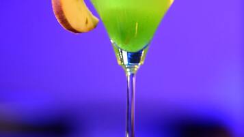 Una copa de martini con un líquido verde y una rodaja de limón en la barra.