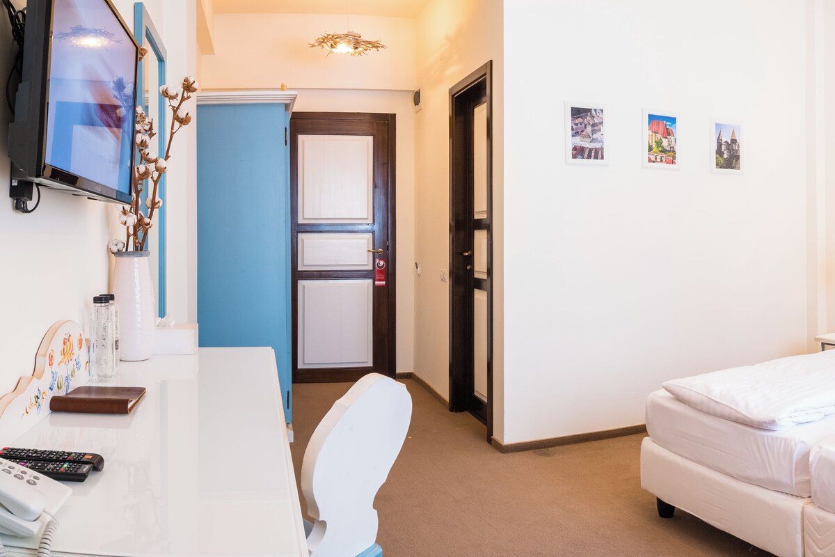 A hotel room with a bed, bedside tables, a desk with a chair, a TV, and a door.