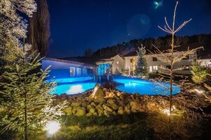 Vista nocturna de una zona residencial con piscina, rodeada de árboles y casas.