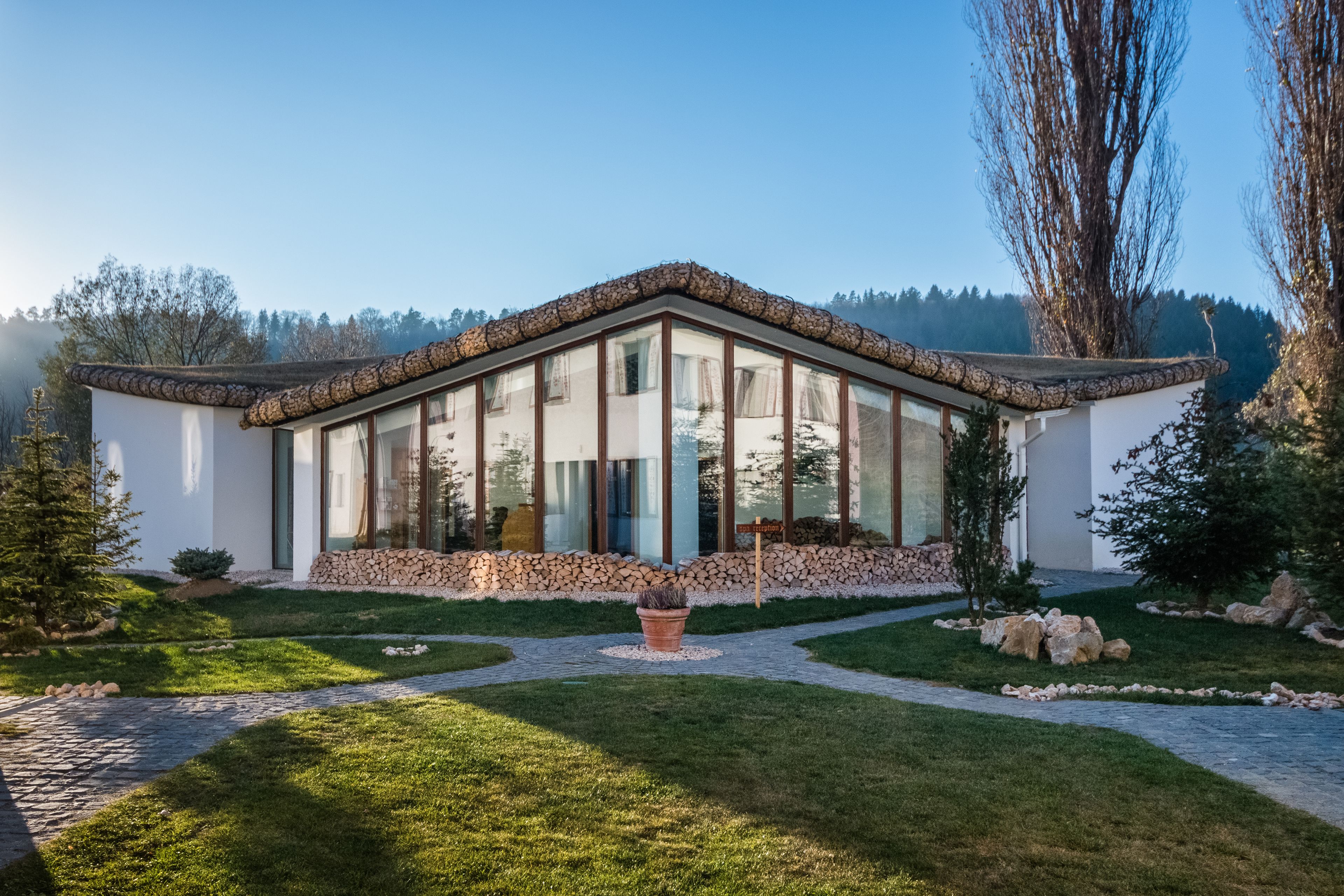 Una casa moderna con base de piedra, grandes ventanales y techo de la misma material.