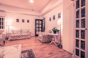 Un amplio salón con un sofá floral, una mesa redonda con una planta y una estantería.