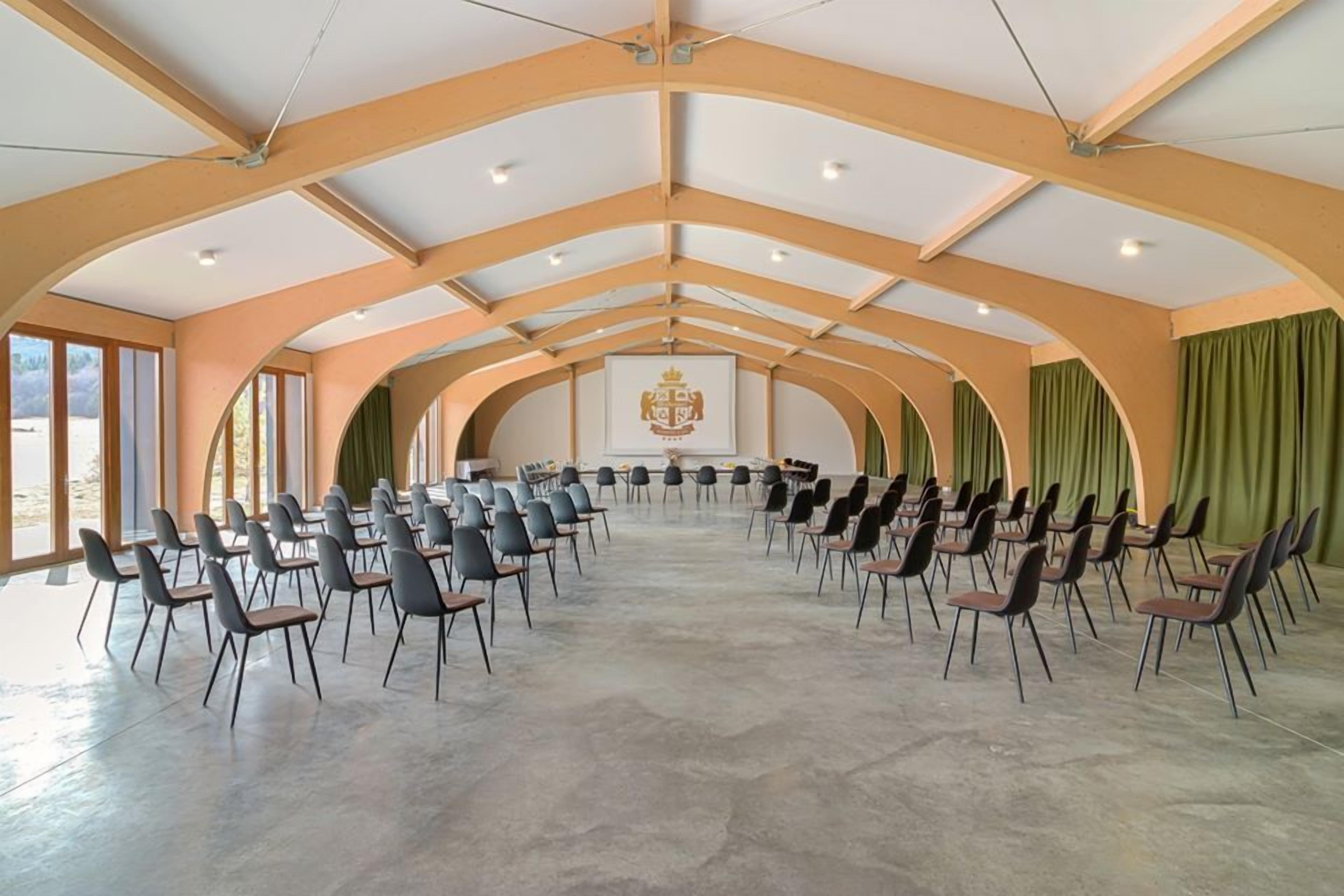 A conference room with a high ceiling, arched ceiling design, and a central emblem. Rows of chairs are arranged for seating.