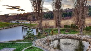 A pond surrounded by a stone border, a small building with a sloped roof, and a grassy area with trees and shrubs. - Wolkendorf Bio Hotel & Spa (Vulcan)