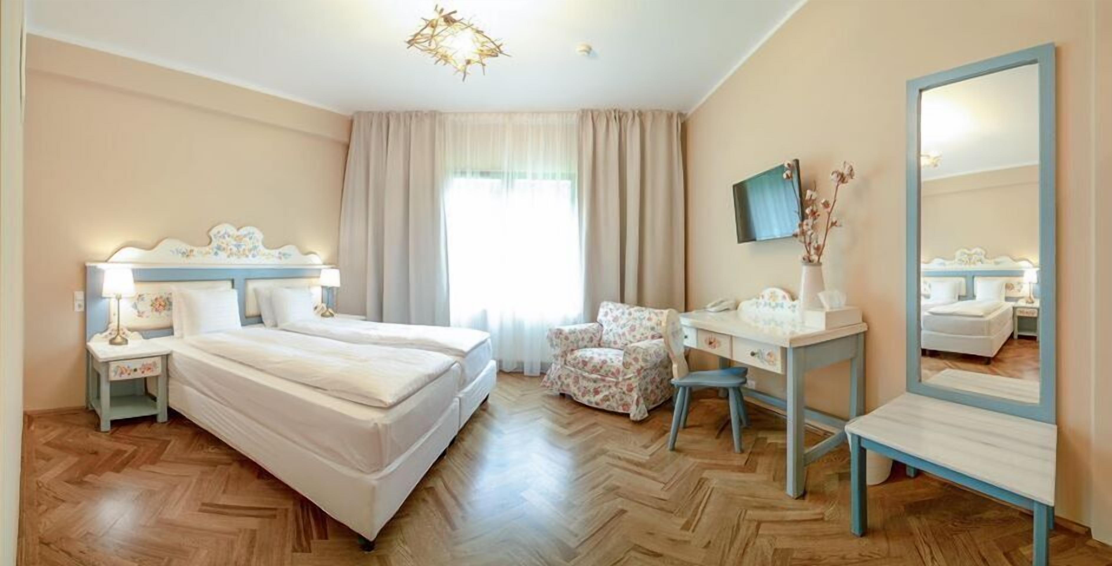 A hotel room with a double bed, a desk with a chair, a mirror, and a television on the wall.