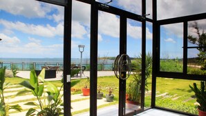 A conservatory with a view of a grassy area and a body of water. - Villa Iris (Baisha)
