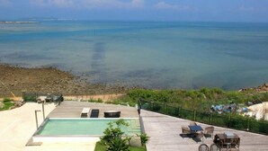A pool area with a view of the ocean, outdoor seating, and a wooden deck. - Villa Iris (Baisha)