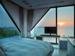 A modern bedroom with a large bed, a television, and a view of the sunset over the water. - Villa Iris (Baisha)